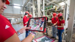 Four people hold ipads and interact with an AR pad in a feed mill