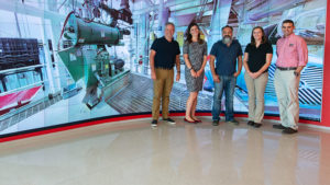 Five people standing in front of a very large screen wall
