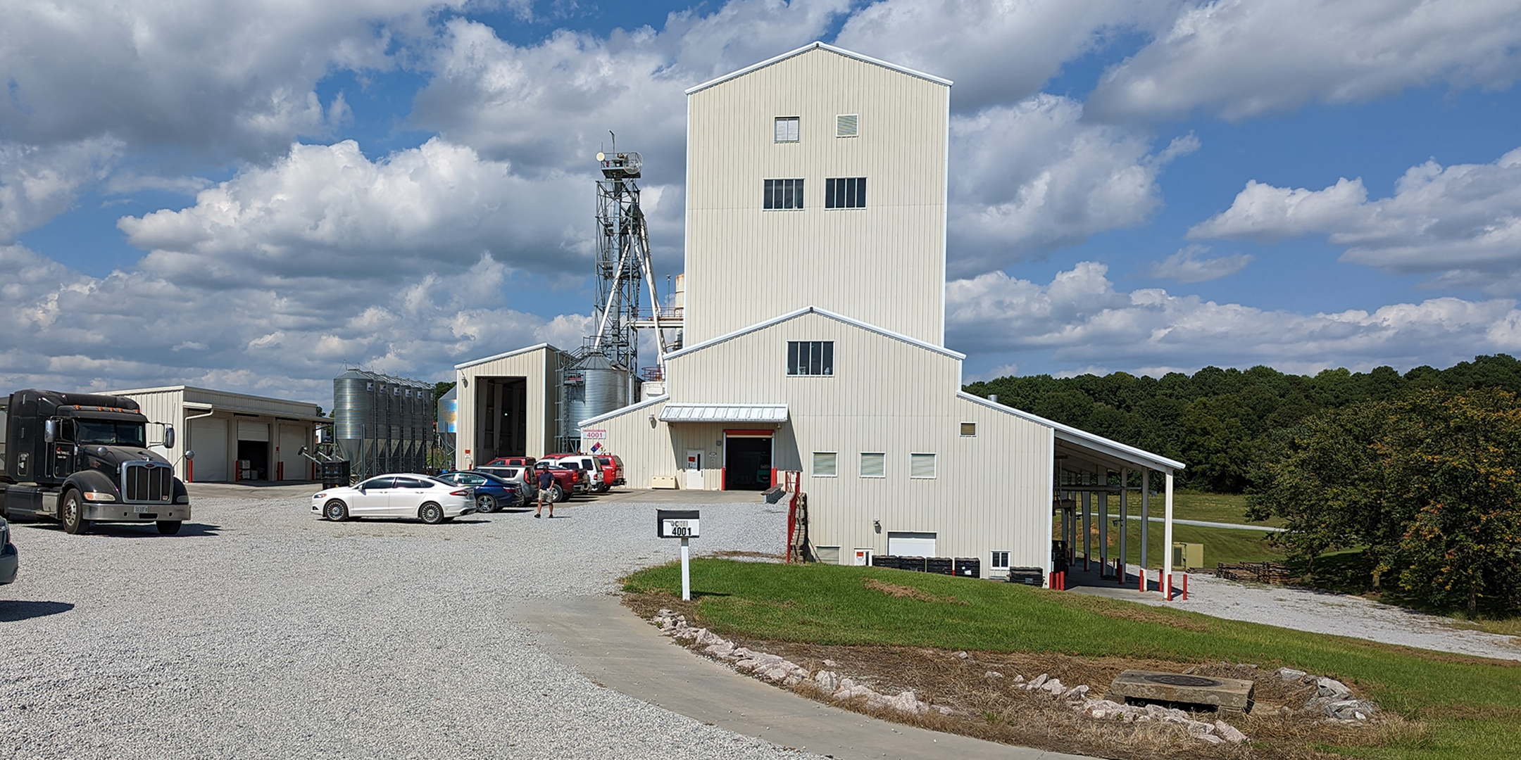 A feed mill with cars and trucks in the parking lot outside.